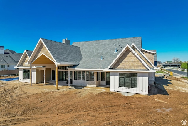 rear view of house featuring roof with shingles, a patio area, a chimney, and board and batten siding