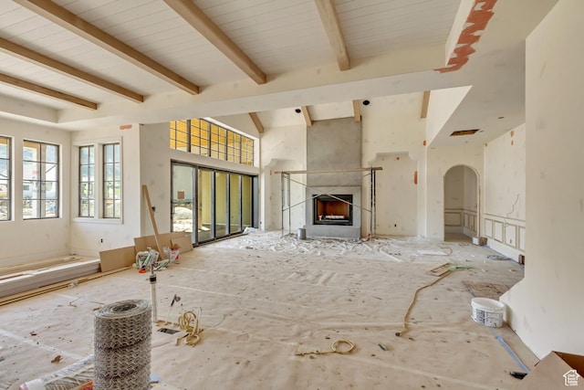 unfurnished living room featuring arched walkways, beamed ceiling, and a high end fireplace