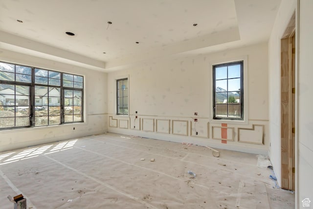 empty room featuring a wainscoted wall, a decorative wall, and a raised ceiling