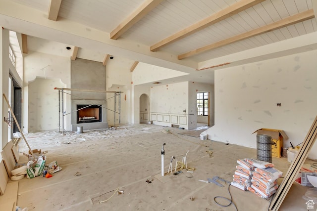 unfurnished living room featuring a high end fireplace, beamed ceiling, arched walkways, and high vaulted ceiling