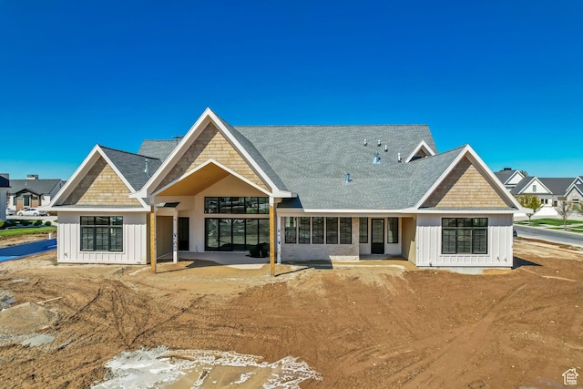 rear view of house featuring a patio area, a shingled roof, and board and batten siding