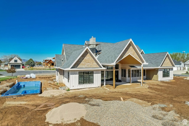 back of property with a shingled roof, board and batten siding, and a chimney