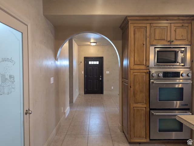 3006 E Somerset Dr, Spanish Fork, UT 84660 - kitchen with arched walkways, multiple ovens, brown cabinets, stainless steel microwave, and light tile patterned flooring