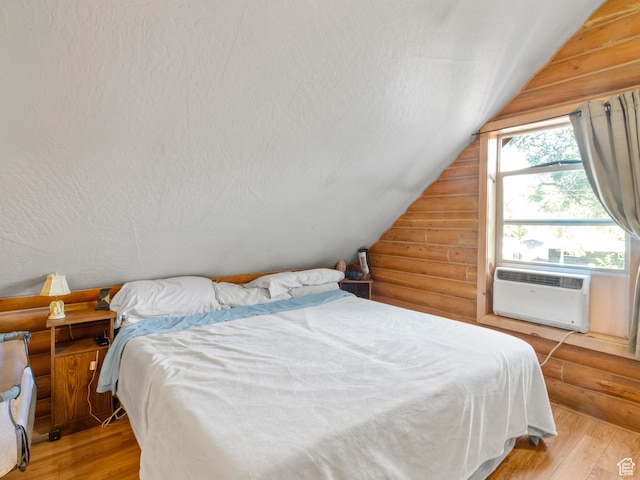 bedroom with light wood-type flooring, log walls, a textured ceiling, and lofted ceiling