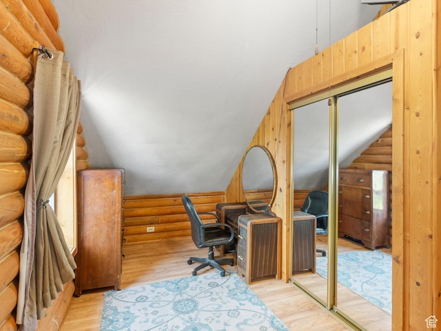 office area featuring lofted ceiling, light wood-style floors, and rustic walls