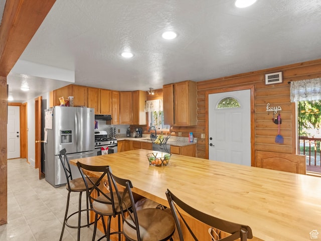 kitchen featuring stainless steel appliances, visible vents, brown cabinetry, a textured ceiling, and under cabinet range hood