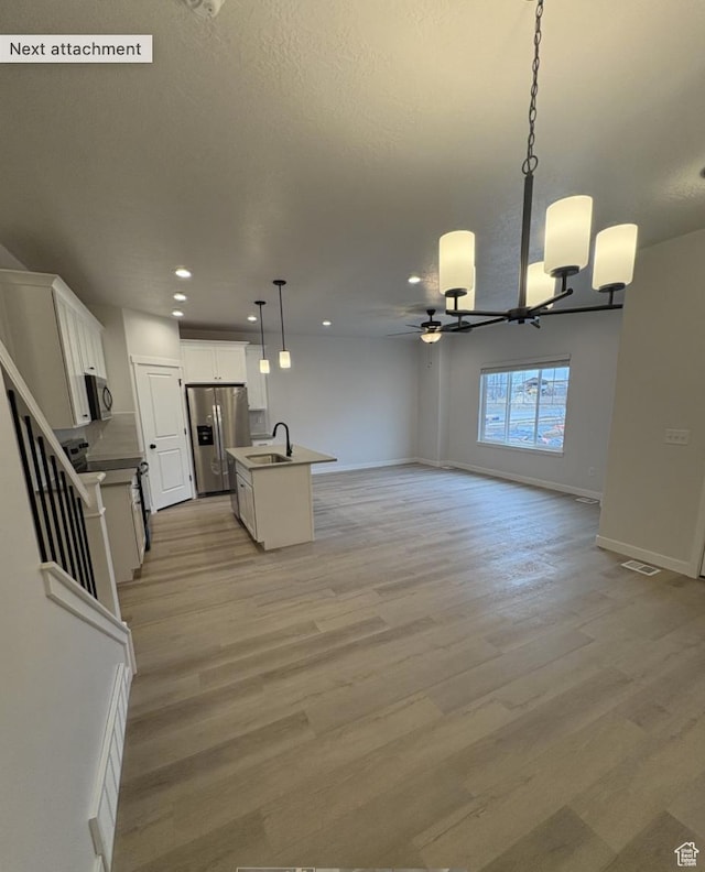 kitchen with a center island with sink, decorative light fixtures, sink, appliances with stainless steel finishes, and white cabinets