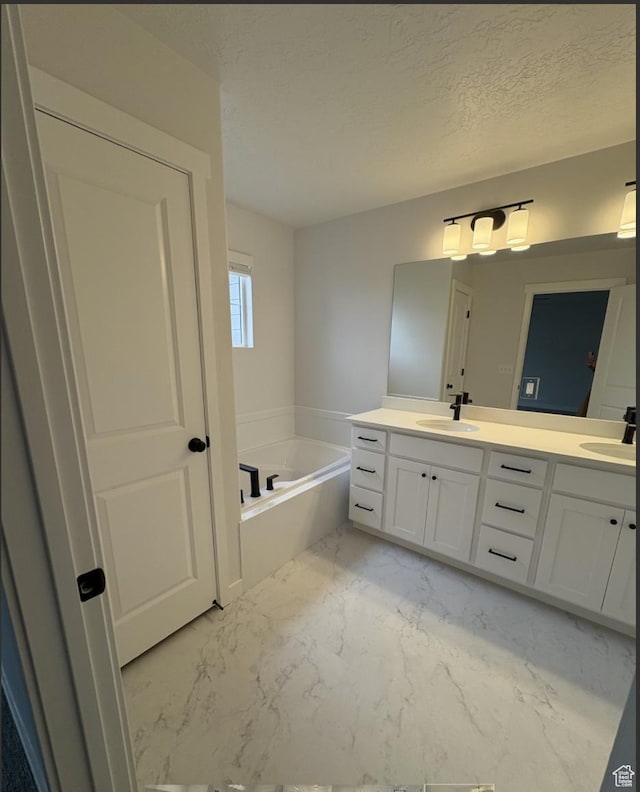 bathroom with a textured ceiling, a bathing tub, and vanity
