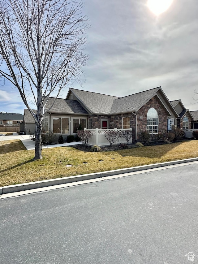 view of front of property featuring stone siding, a front lawn, and roof with shingles