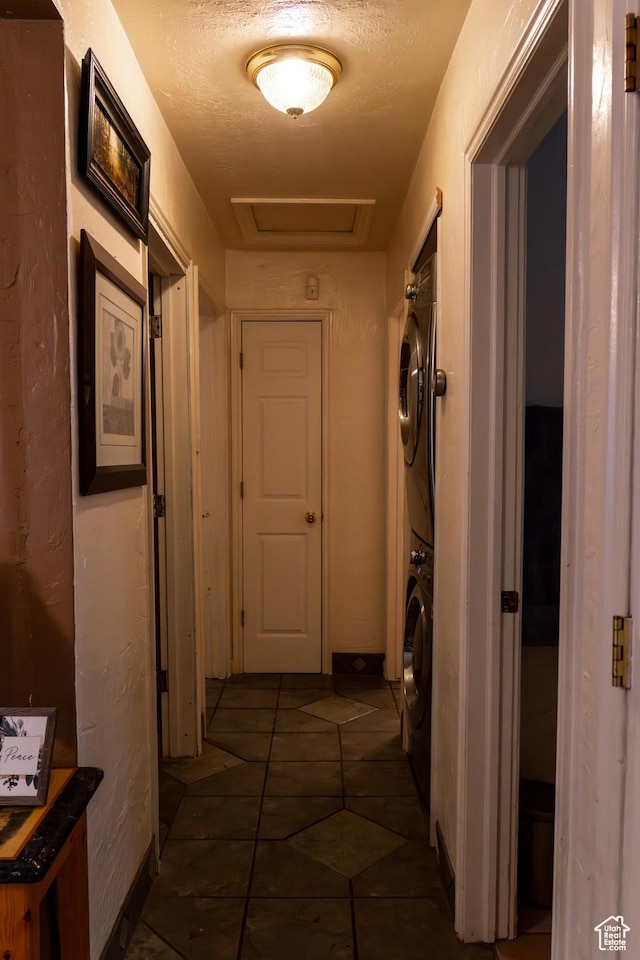 hall featuring a textured ceiling, dark tile patterned floors, and stacked washer and clothes dryer