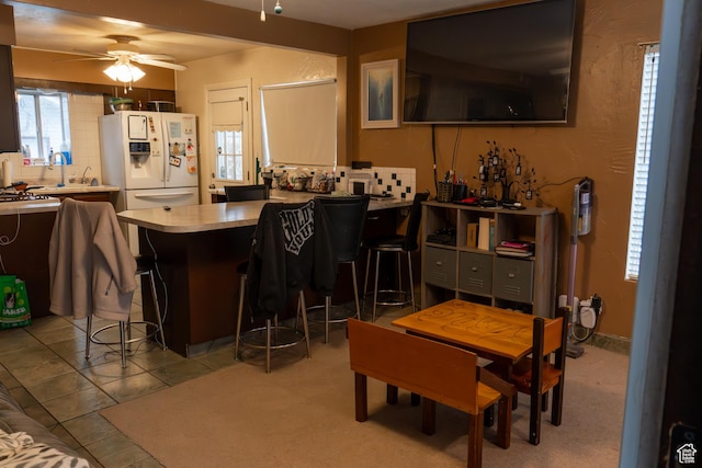 bar with white refrigerator with ice dispenser, ceiling fan, plenty of natural light, and light tile patterned floors