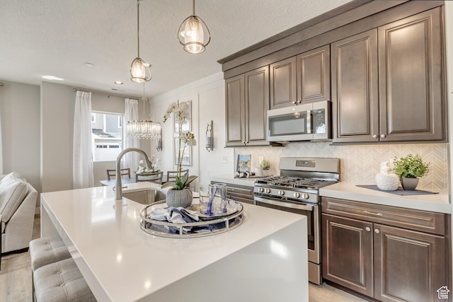 3791 S 3235 W Unit 15, West Haven, UT 84401 - kitchen featuring pendant lighting, stainless steel appliances, dark brown cabinets, a kitchen island with sink, and decorative backsplash