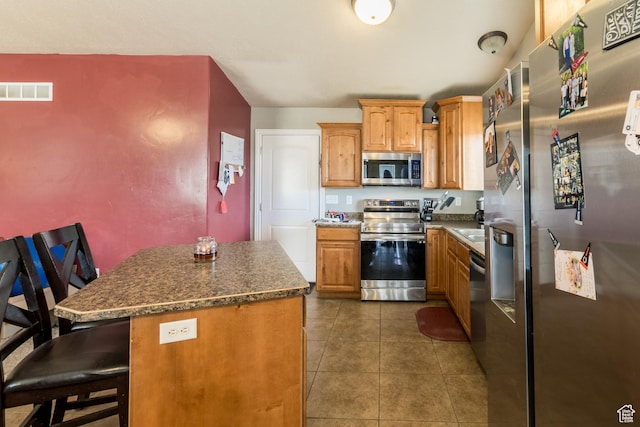 kitchen featuring appliances with stainless steel finishes, a kitchen island, dark tile patterned flooring, and a breakfast bar area