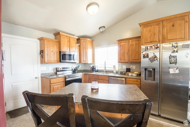 kitchen with appliances with stainless steel finishes, sink, vaulted ceiling, light tile patterned floors, and a kitchen island