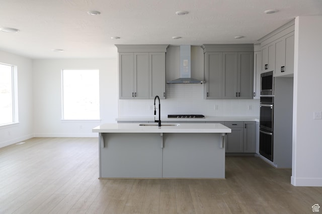 2895 E Liam Ln Unit 106, Eagle Mountain, UT 84005 - kitchen with gray cabinets, wall chimney exhaust hood, stainless steel microwave, light countertops, and a kitchen island with sink
