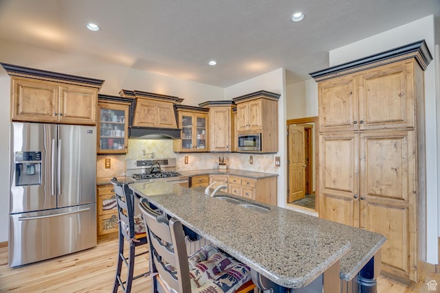kitchen with stainless steel appliances, light stone countertops, a sink, and glass insert cabinets