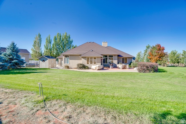 rear view of property featuring an outdoor structure, a lawn, a storage unit, a chimney, and a patio
