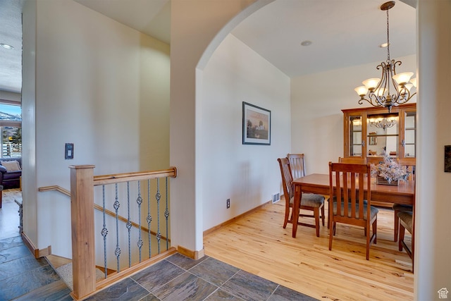 dining space with baseboards, a notable chandelier, stone tile floors, and arched walkways