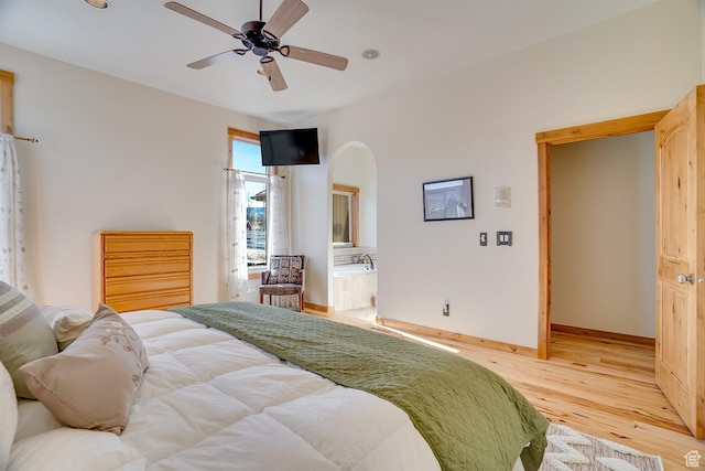 bedroom featuring baseboards, arched walkways, wood finished floors, ensuite bathroom, and a ceiling fan