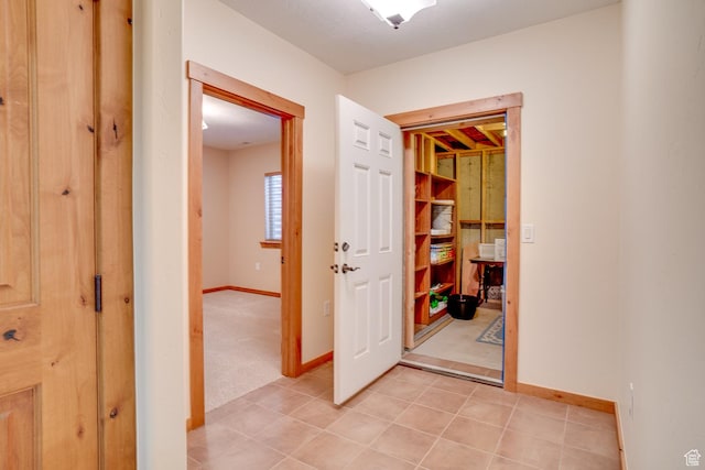 hallway featuring baseboards, light colored carpet, and light tile patterned floors