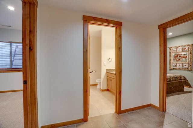hall featuring baseboards, visible vents, light colored carpet, and light tile patterned flooring
