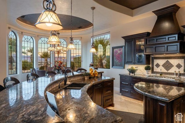 2024 W 450th Cir S, St George, UT 84770 - kitchen featuring dark stone countertops, a raised ceiling, an island with sink, a sink, and decorative light fixtures