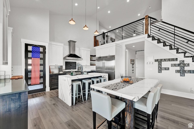 2673 S 4950 W, Taylor, UT 84401 - kitchen with built in fridge, a breakfast bar area, white cabinets, wall chimney range hood, and an island with sink