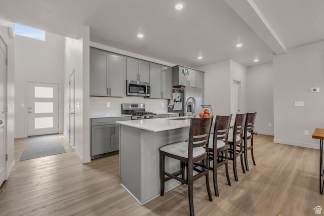 kitchen with appliances with stainless steel finishes, gray cabinets, a center island with sink, and a kitchen breakfast bar