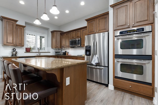 3013 W Alta Peak Rd, South Jordan, UT 84095 - kitchen featuring light stone counters, light wood-style flooring, a breakfast bar, appliances with stainless steel finishes, and a center island