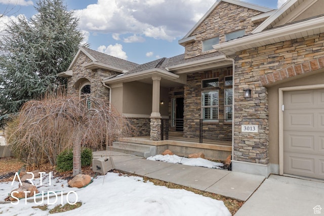 3013 W Alta Peak Rd, South Jordan, UT 84095 - snow covered property entrance featuring stone siding, a porch, an attached garage, and stucco siding