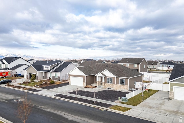 view of front of property featuring a garage, fence, stone siding, driveway, and a residential view