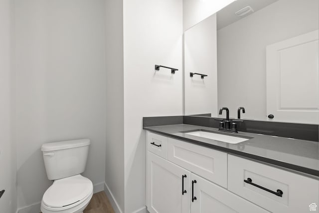 half bathroom with visible vents, toilet, vanity, wood finished floors, and baseboards
