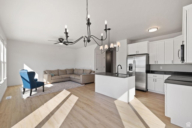 kitchen with a center island with sink, dark countertops, appliances with stainless steel finishes, light wood-style floors, and open floor plan