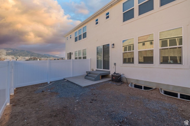 back of house featuring central air condition unit, fence, a mountain view, and stucco siding