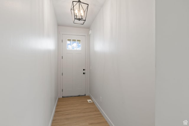 doorway with a chandelier, baseboards, visible vents, and light wood finished floors