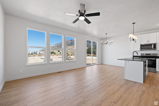 kitchen featuring white cabinets, dark countertops, appliances with stainless steel finishes, open floor plan, and light wood-type flooring