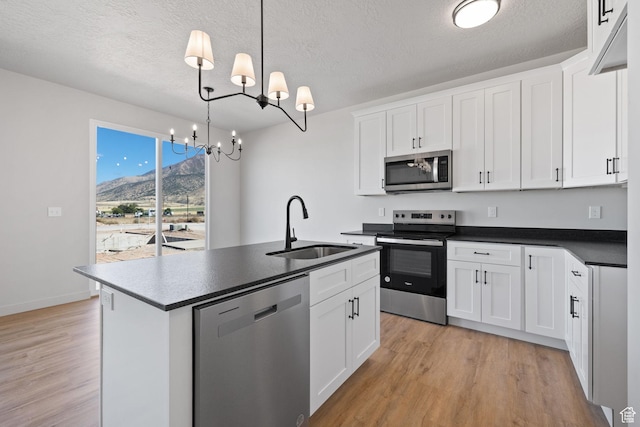 kitchen with dark countertops, light wood-style flooring, appliances with stainless steel finishes, white cabinetry, and a sink