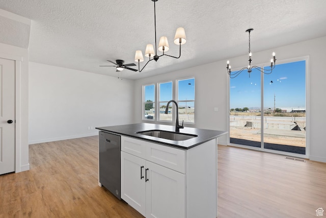 kitchen featuring dark countertops, visible vents, stainless steel dishwasher, a sink, and light wood-type flooring