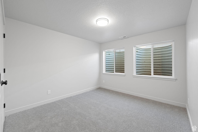empty room with a textured ceiling, carpet, visible vents, and baseboards