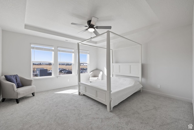 carpeted bedroom featuring a ceiling fan, baseboards, a tray ceiling, and a textured ceiling