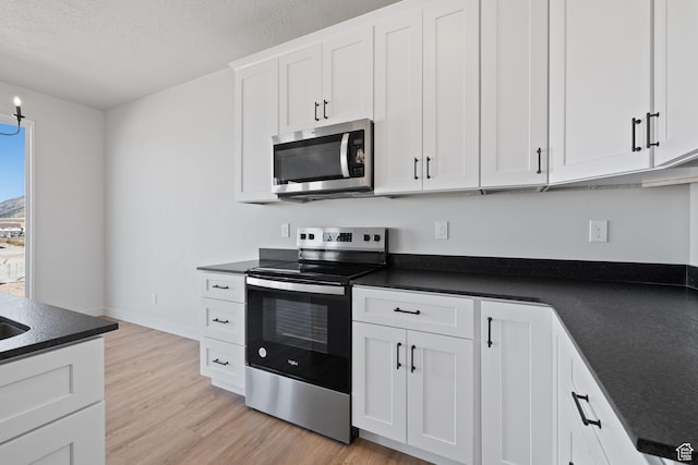 kitchen featuring dark countertops, stainless steel appliances, a textured ceiling, light wood-type flooring, and white cabinetry