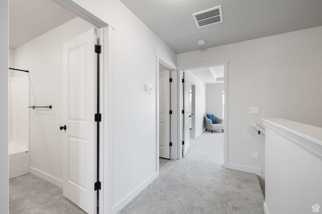 hall featuring visible vents, light carpet, baseboards, and a textured ceiling