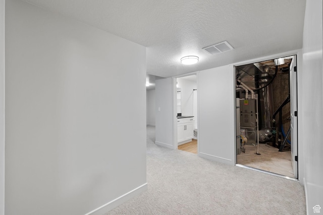 basement with baseboards, visible vents, light carpet, and a textured ceiling