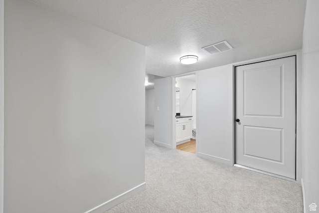 interior space with a textured ceiling, baseboards, visible vents, and light colored carpet