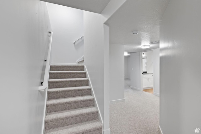 stairway featuring a textured ceiling, carpet, and baseboards