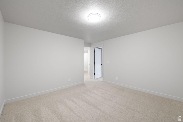 spare room with baseboards, a textured ceiling, and light colored carpet