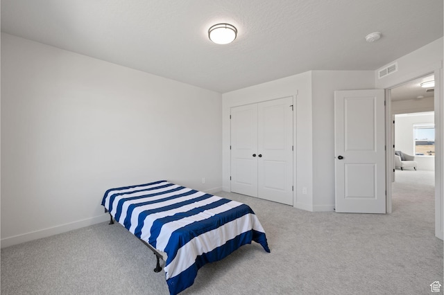 carpeted bedroom with baseboards, a textured ceiling, visible vents, and a closet