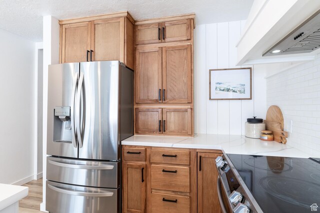 93 N 200 W, Smithfield, UT 84335 - kitchen featuring light wood finished floors, decorative backsplash, brown cabinetry, appliances with stainless steel finishes, and custom exhaust hood