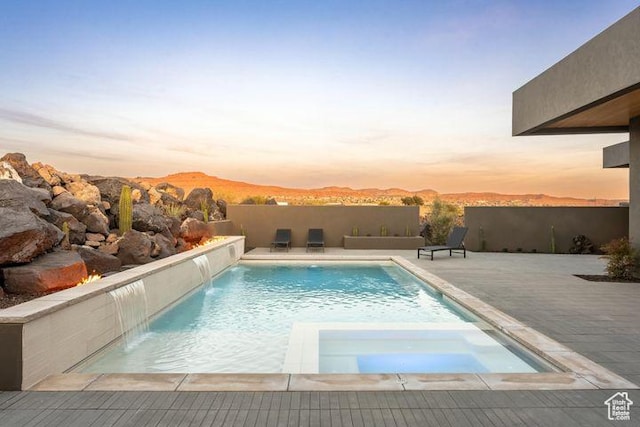 2655 W Shoshoni Trl, St George, UT 84770 - pool at dusk featuring a pool with connected hot tub, fence, a mountain view, and a patio