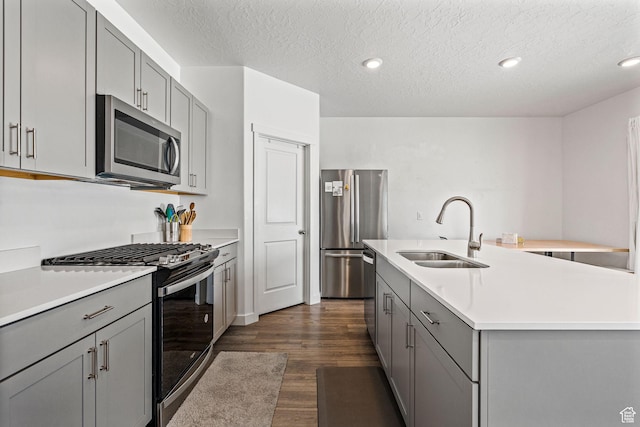 kitchen with dark wood-style floors, stainless steel appliances, light countertops, a kitchen island with sink, and a sink